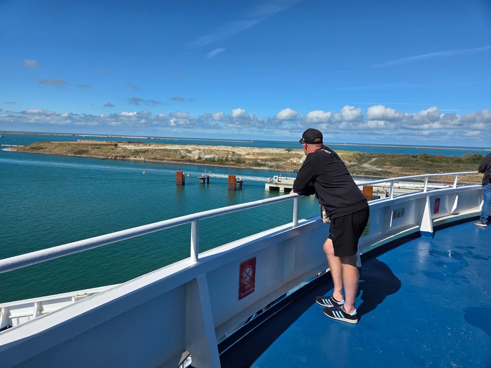 One of our group leaning on the railing of a blue upper deck, looking out over Dunkirk harbour