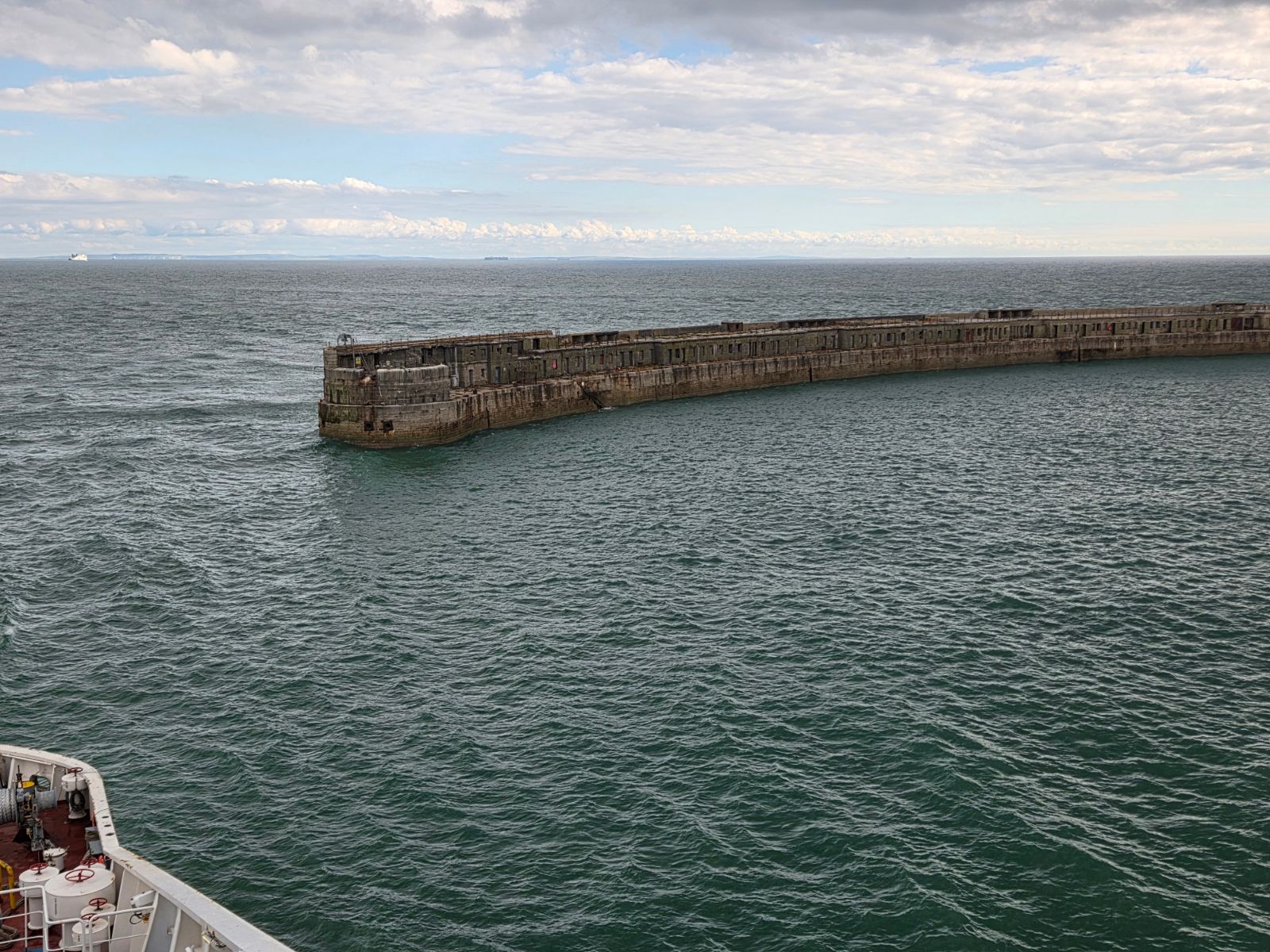 Stone harbour wall at Dover seen from the ferry, with grey-green sea and a distant ferry