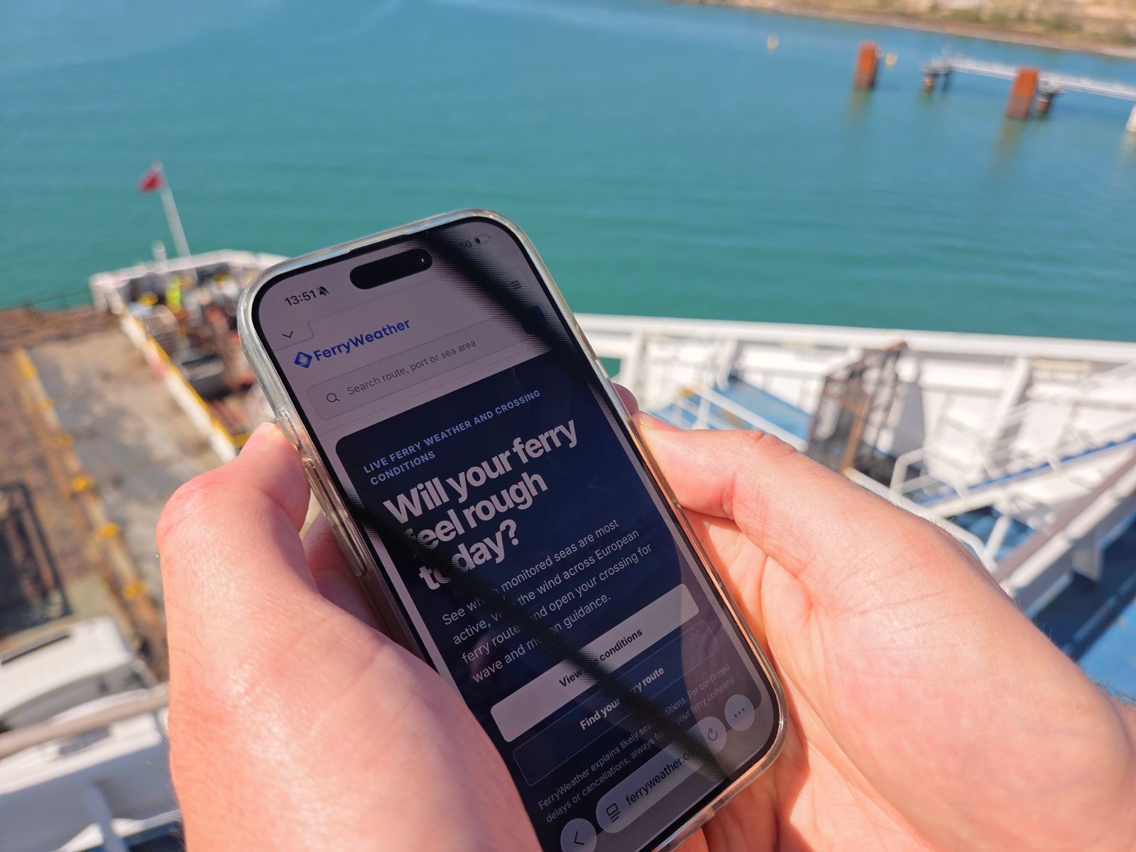 Phone showing the FerryWeather crossing conditions page, held above the deck of Delft Seaways in Dunkirk harbour