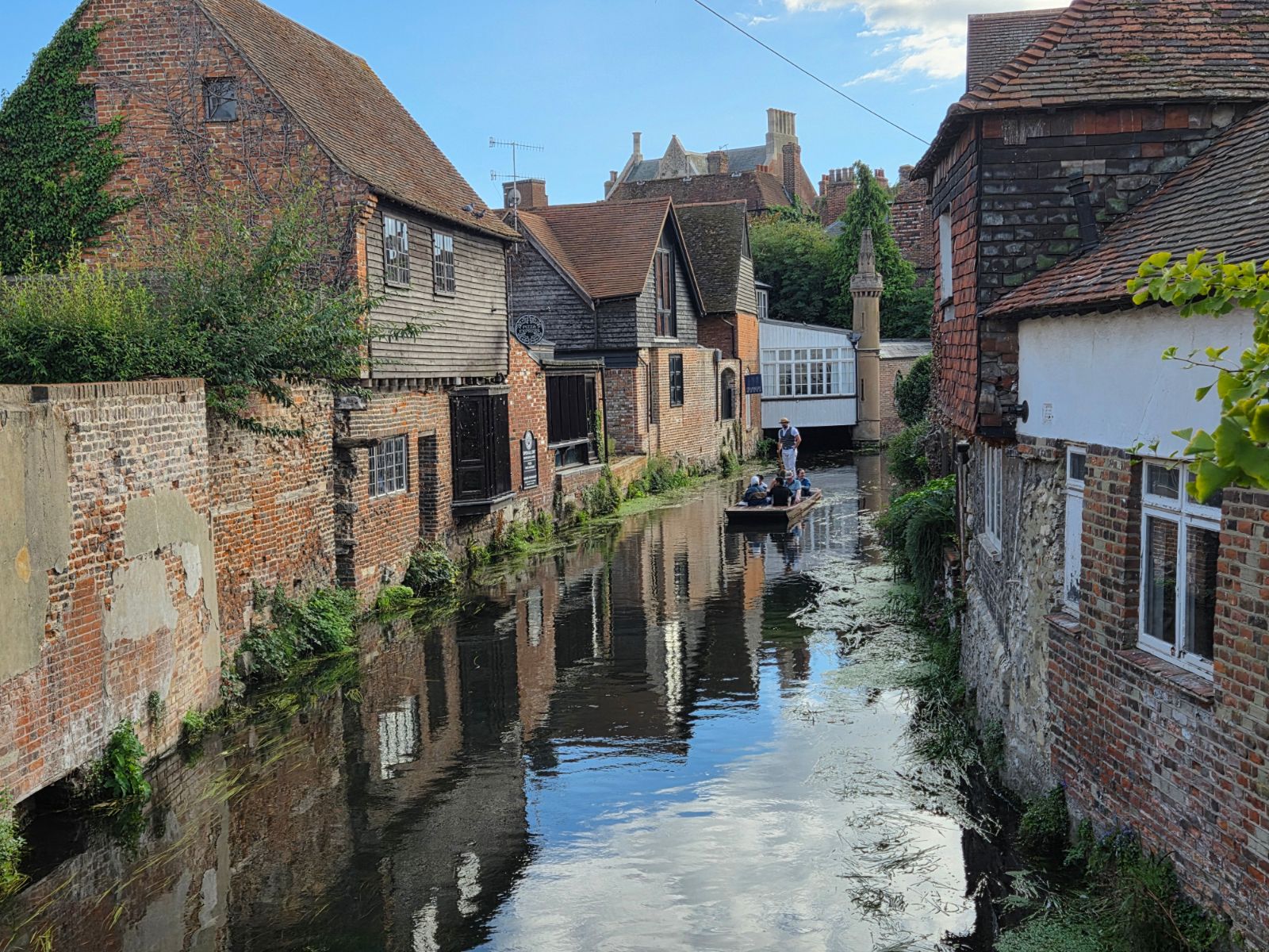Punt with passengers on the River Stour in Canterbury, between old brick and tile-hung buildings reflected in the water